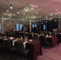 Rows of tables covered in dark cloths create a formal setting in a dimly lit hall, providing space for group gatherings.